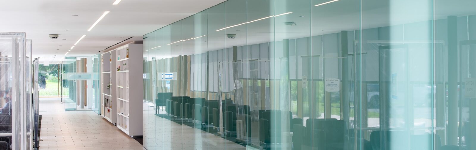 Modern corridor with transparent glass walls and seating area.