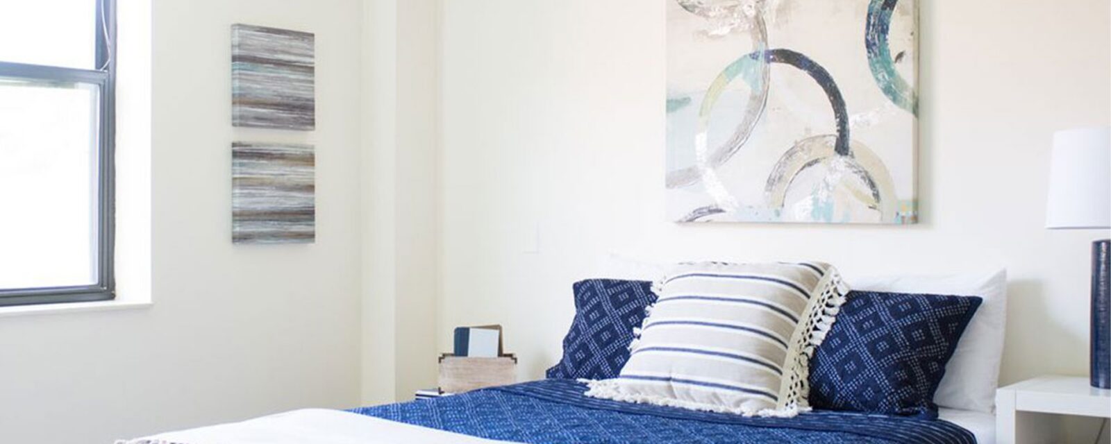 Cozy bedroom with blue bedding and abstract wall art.