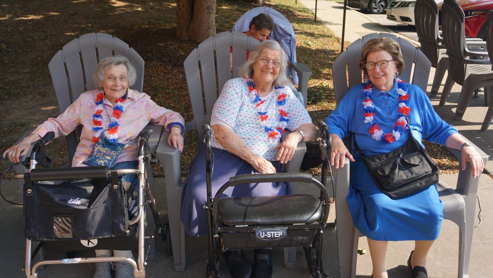 Three elderly women smiling, wearing leis, sitting outdoors.